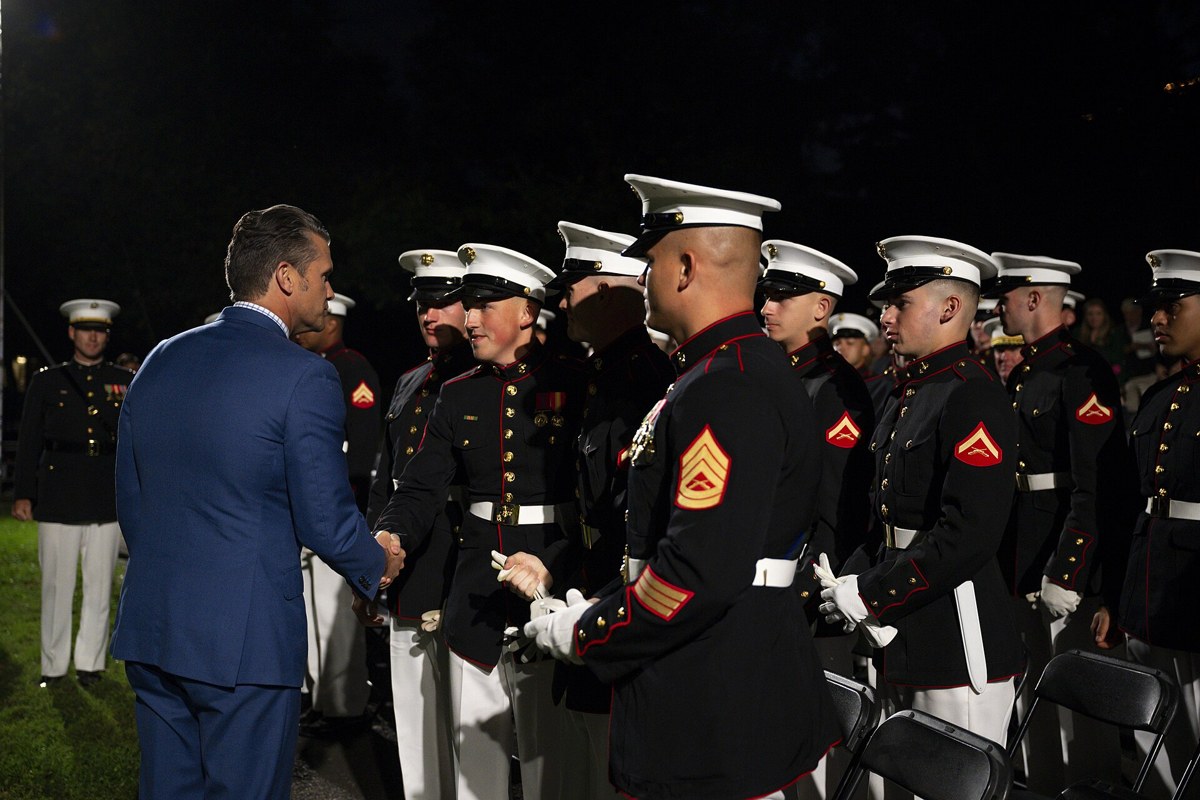 Pete Hegseth shakes hands with Marines in dress blues during a night ceremony